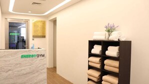 Zona de recepción con mostrador de mármol que indica “ENERGY GYM” y un estante con toallas dobladas ordenadamente.