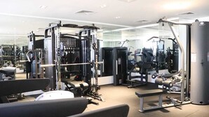 Un gimnasio con diferentes máquinas de ejercicio, bancos y un espejo grande.