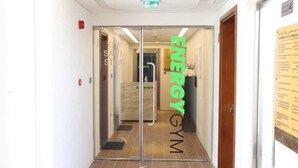 Un pasillo que conduce a un gimnasio con una puerta de vidrio, un detector de incendios y un letrero con el nombre del gimnasio.