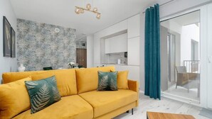 A modern living room with a yellow sofa, a wooden coffee table, and a kitchen in the background.