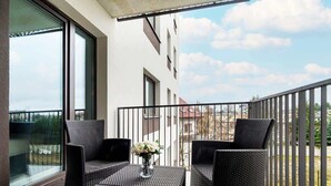A balcony with two wicker chairs and a small table, a vase with flowers, and a view of buildings and trees.