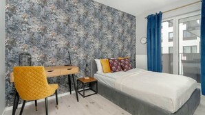 A bedroom with a bed, a desk, a chair, and a large window with curtains.
