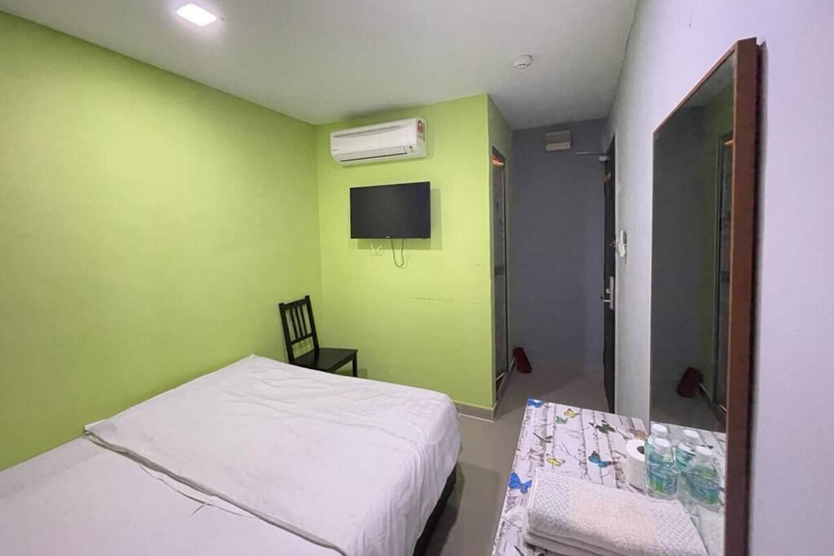A bedroom with a bed, a chair, a TV, and an air conditioning unit.
