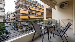 A balcony with a table and chairs, overlooking a street with cars and buildings. - Chic and Lavish Apartment in Athens (Kallithea)