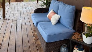 A covered porch with a blue sofa, a wicker chair, and a table with a lamp and a plant. - Eaglewatch Mountaintop Cabin (Bryson City)