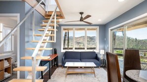 A modern living room with a staircase, a sofa, a coffee table, and a view of the outdoors. - Eaglewatch Mountaintop Cabin (Bryson City)