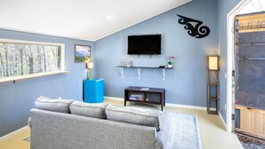 Un soggiorno con un divano grigio, un mobiletto blu, una TV a parete e un elemento decorativo a parete.