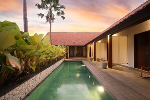 A poolside area with a wooden deck, a tiled roof, and a row of doors. - Rarama Living Studio (Kerobokan Kaja)
