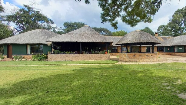 A building with thatched-roof structures, a central open area, and surrounding greenery. - ZIMPARKS BOOKINGS (Hammanskraal)