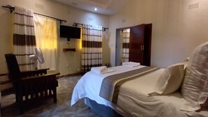 A hotel room with a bed, a desk, a chair, a TV, and a bathroom with a shower curtain. - ZIMPARKS BOOKINGS (Hammanskraal)