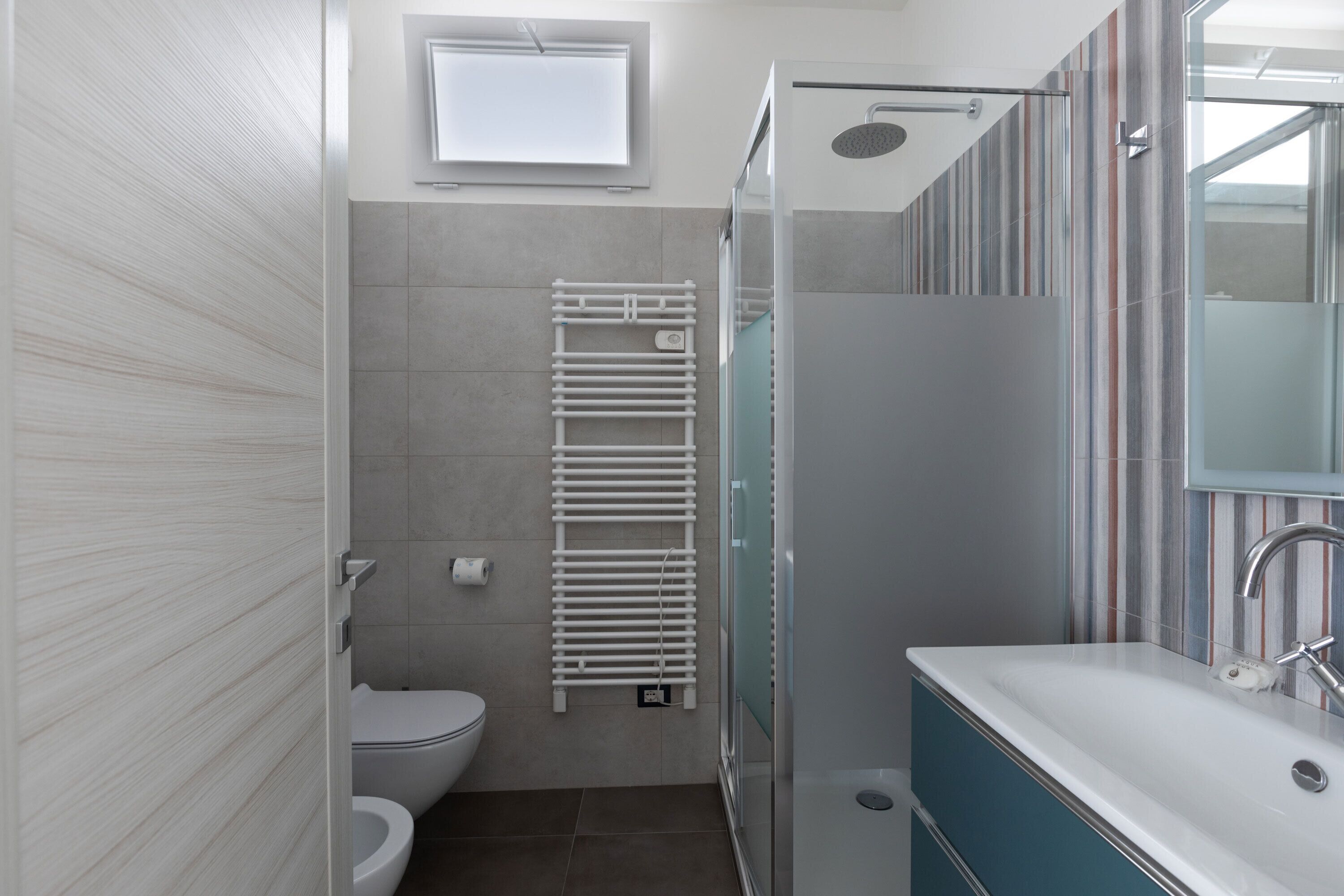 A modern bathroom with a toilet, a glass shower enclosure, a white sink, and a towel rack.