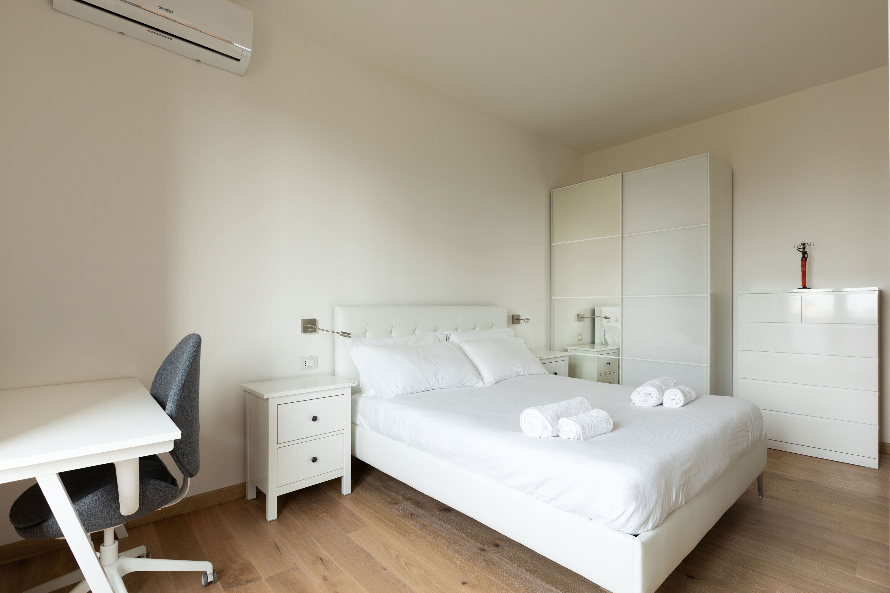 A bedroom with a bed, a desk, a chair, a nightstand, a wardrobe, and a mirror.