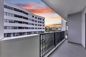 A modern building with a balcony overlooking a sunset.