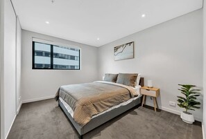 A bedroom with a large bed, a nightstand, a bedside table, a window, and a potted plant.