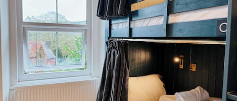 A bunk bed room with a window, a radiator, and a curtain.