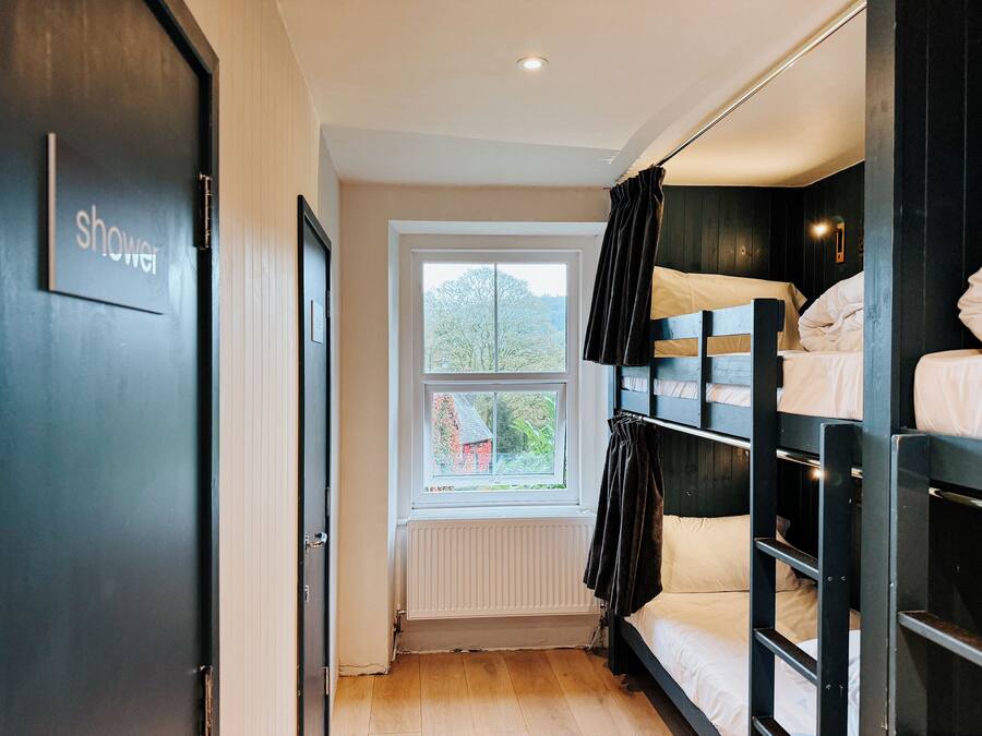 A room with a bunk bed, a window with a view of greenery, a radiator, and a door labeled "shower".