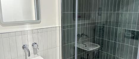 Un baño con lavamanos blanco, un espejo y una zona de ducha con azulejos oscuros.