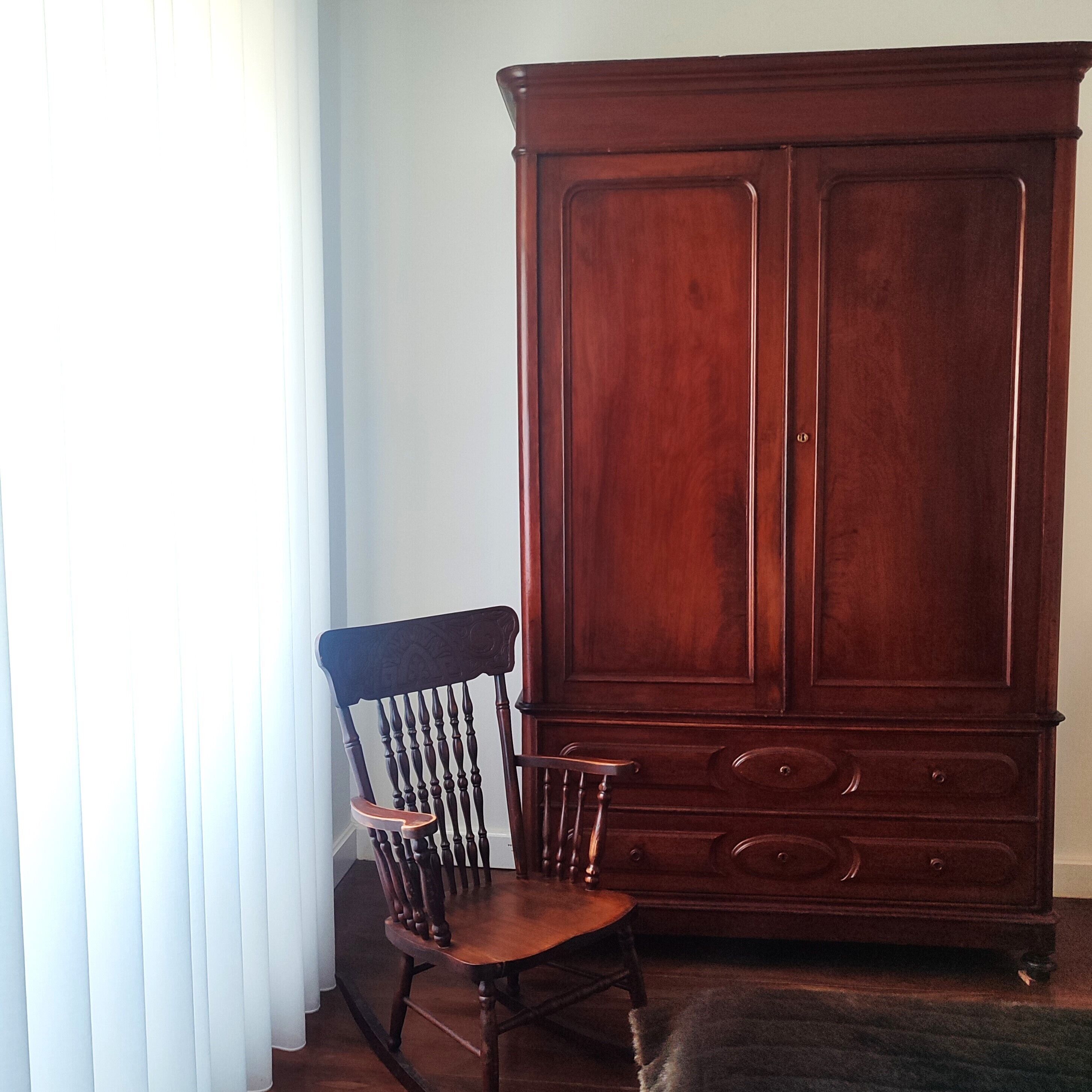 A wooden chair with a cushioned seat and backrest, positioned next to a large wooden cabinet with two doors and several drawers.
