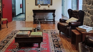A living room with a wooden floor, a red door, a fireplace, a leather armchair, and a painting on the wall. - Quinta dos Mistérios  (Velas)