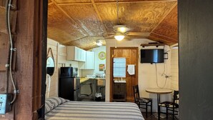 Une pièce confortable comprenant un lit, une petite kitchenette, un coin repas et un téléviseur fixé au mur.