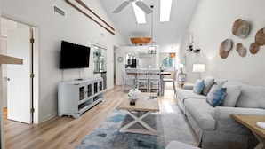 Un salon moderne doté d’un ventilateur de plafond, d’un téléviseur à écran plat, d’un coin repas et d’un canapé gris.