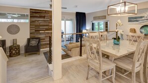 Un salon moderne avec un mur en bois, un coin repas avec une table et des chaises blanches, et un escalier menant à un balcon.
