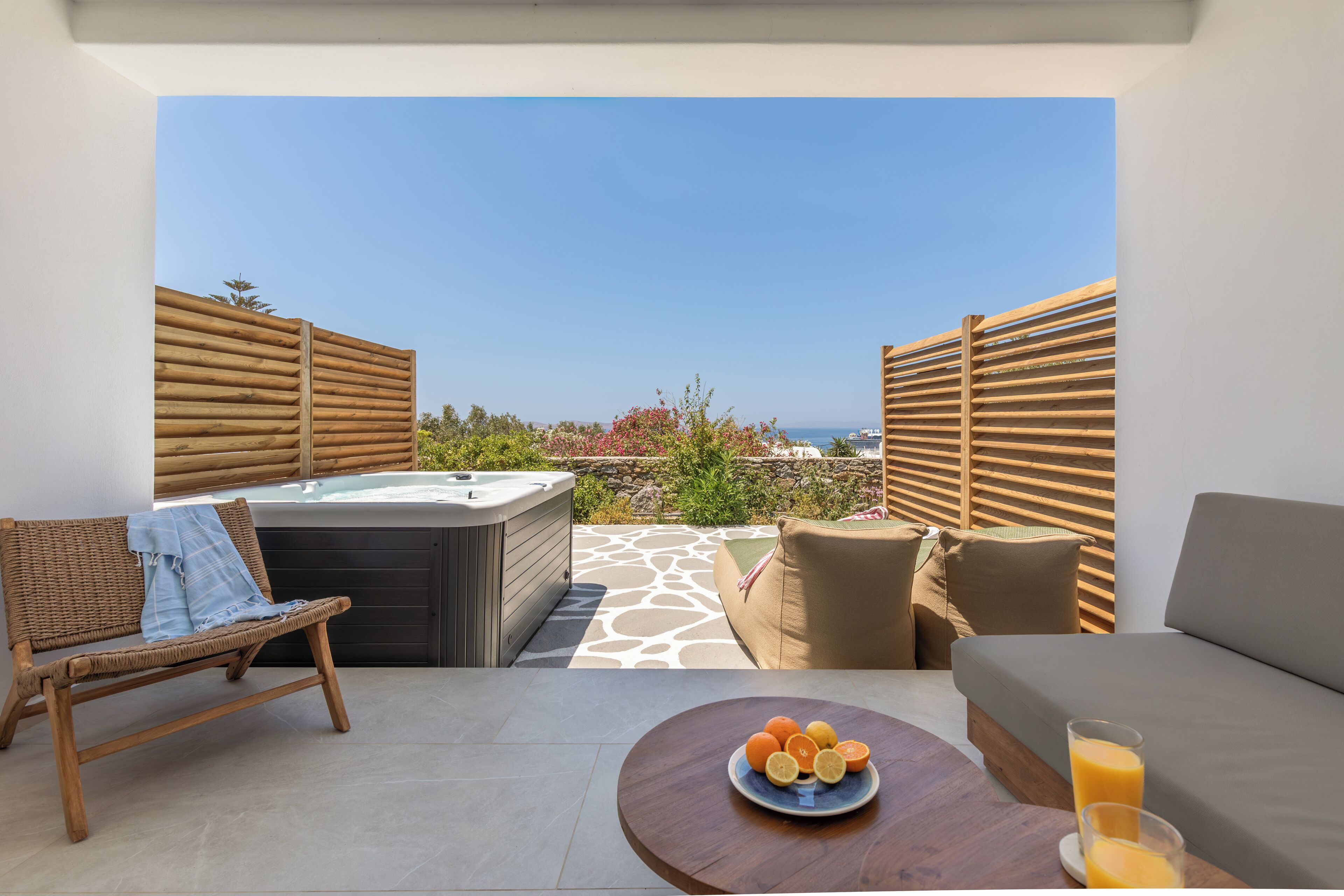 Ein Balkon mit Whirlpool, Korbmöbeln, einer Couch und einem Tisch mit Früchten und einem Glas Orangensaft.