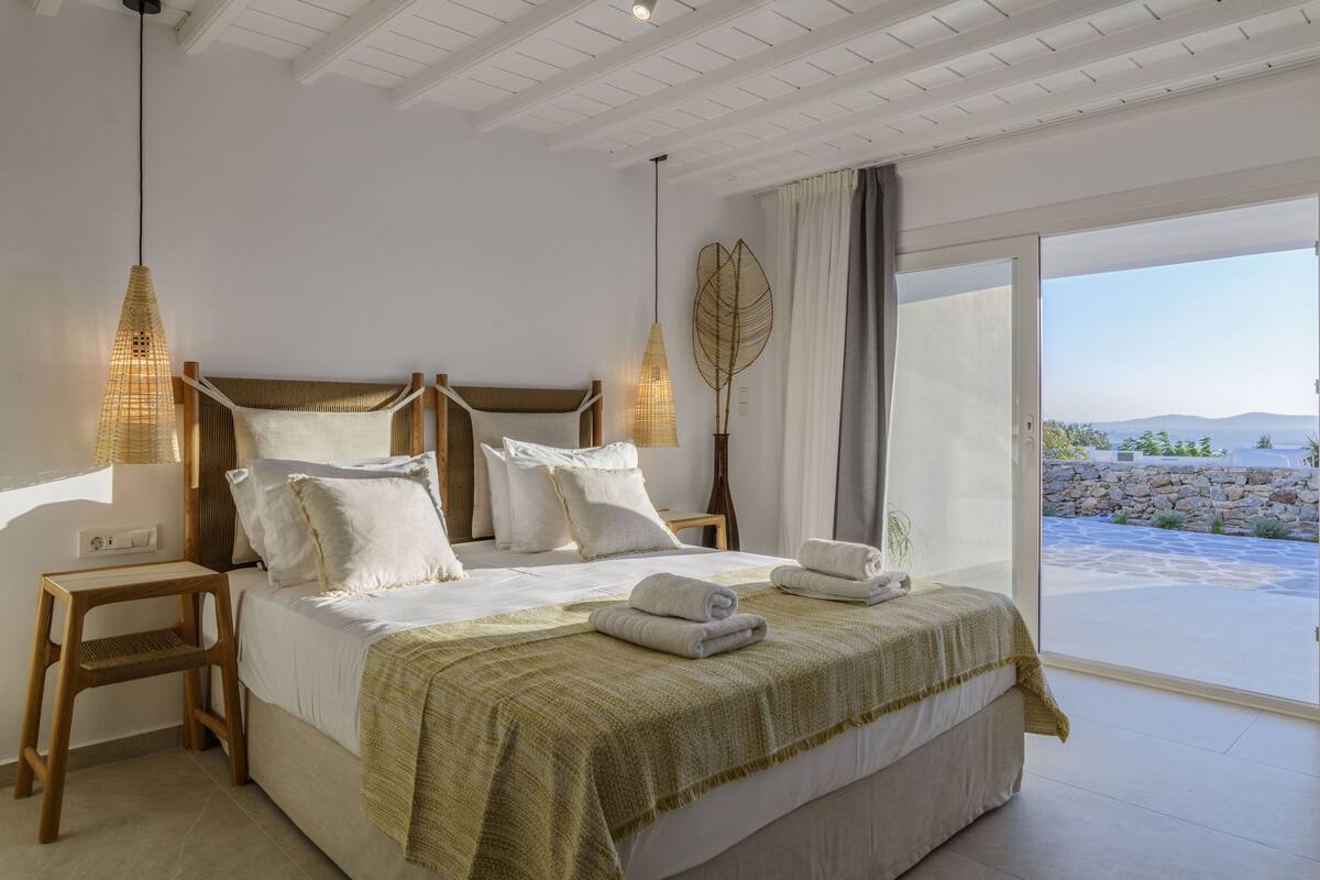 Un dormitorio con una cama grande, cabecera de madera, lámparas de noche, vistas al exterior y un balcón.
