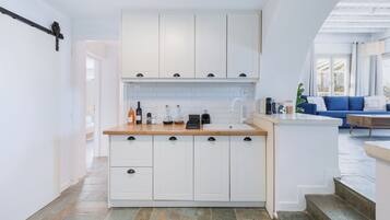 Une cuisine moderne avec des armoires blanches, un plan de travail en bois et un évier encastré. Un escalier mène à un espace extérieur aménagé avec un canapé bleu et une plante.