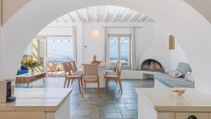 Uma área de refeições acolhedora, com uma mesa, cadeiras, lareira e vista para o mar.