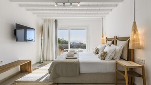Quarto com cama grande, televisão na parede, um banco e vista para o exterior.