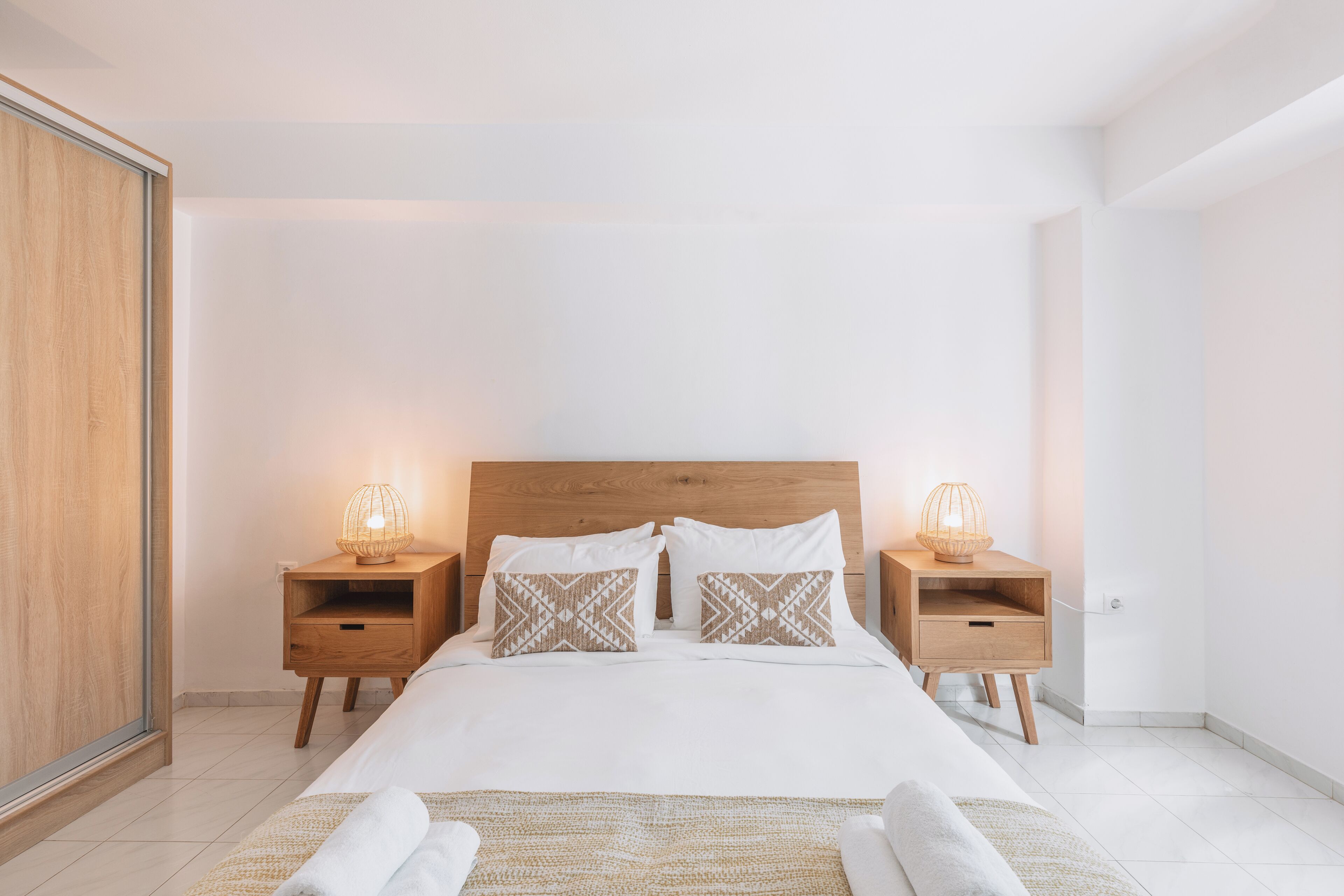 A modern bedroom with a wooden headboard, two bedside tables with lamps, and a large bed with white bedding.