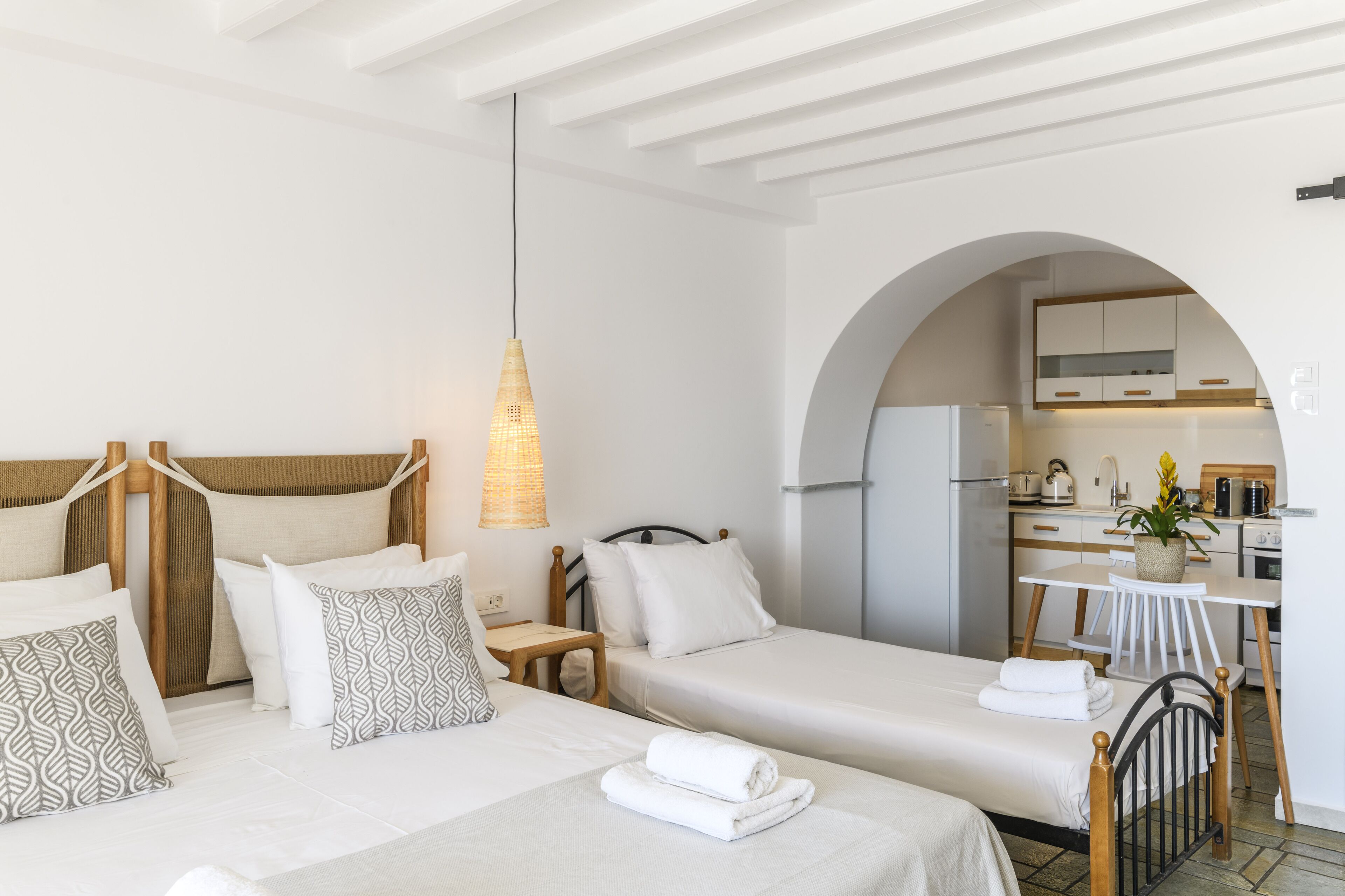 Una habitación de hotel con dos camas, una mesita y una kitchenette.