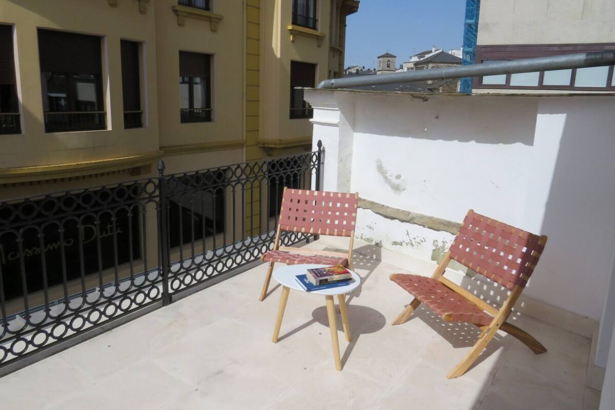 A balcony with two wooden chairs and a small table, surrounded by a metal railing.