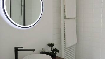 Un baño con un espejo redondo, un lavamanos blanco y un perchero para toallas.