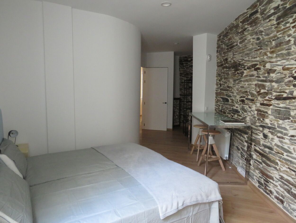 Une chambre à coucher avec un lit, un bureau et un mur en pierre.