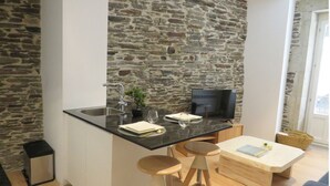 A modern kitchen with a stone wall, a black countertop, a sink, a TV, and wooden stools.