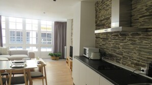 Una cocina moderna con salpicadero de piedra, un comedor con mesa y sillas, y una sala de estar con sofá y ventanas amplias.
