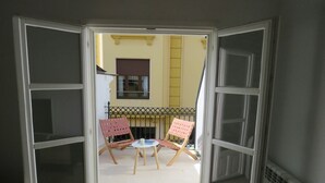 Puerta abierta que da a un balcón con dos sillas y una pequeña mesa.