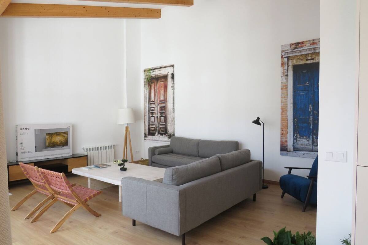A modern living room with a grey sofa, a white coffee table, a wooden floor, a TV, and a blue chair.