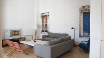 Un saló modern amb un sofà gris, una taula de centre blanca, un terra de fusta, un televisor i una cadira blava.