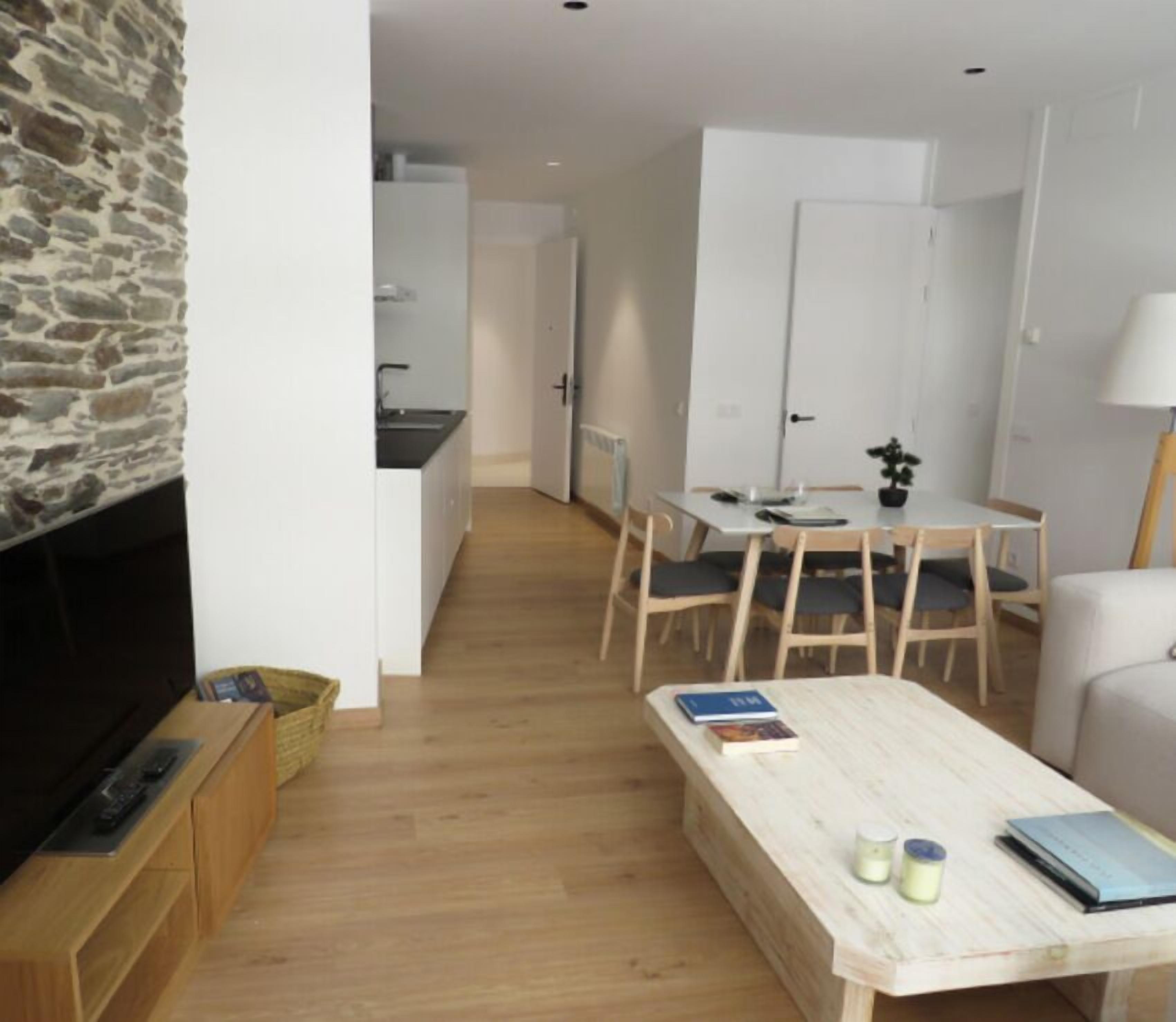 Una sala de estar moderna con una pared de acento de piedra, un televisor de pantalla plana, una mesa de centro de madera y un comedor con una mesa y sillas.