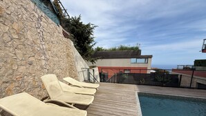 Un espace aménagé au bord de la piscine, avec des chaises longues, un mur en pierre et une vue sur l’océan.
