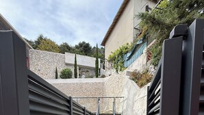 Une entrée fermée par un portail, avec un escalier en métal menant à un mur de pierre.