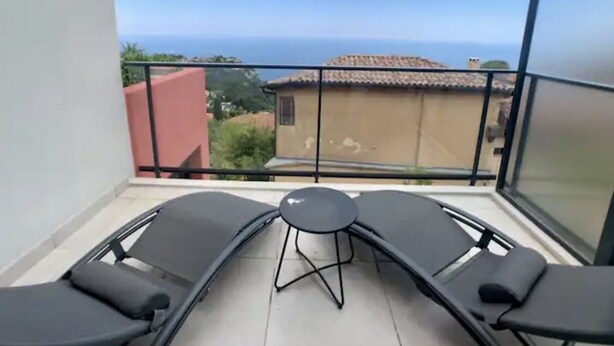 Un balcon avec deux fauteuils et une petite table, offrant une vue sur la côte, avec des bâtiments et de la végétation.