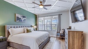 Un dormitorio con cama, mesita de noche, cómoda, ventilador de techo y un ventanal con cortinas.