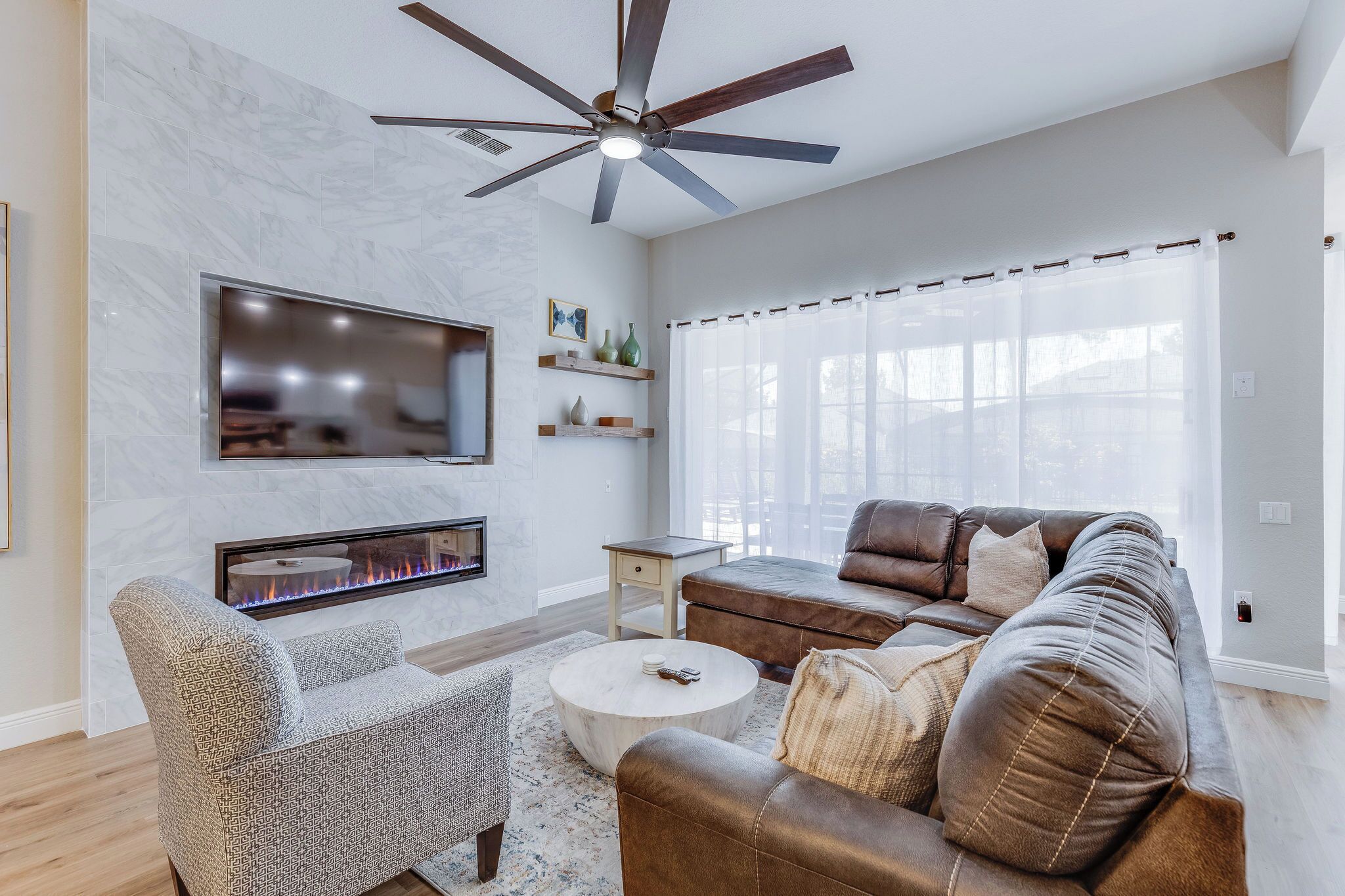 Una sala de estar moderna con chimenea, sofá de cuero y ventilador de techo.