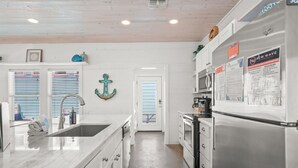 A kitchen with a stainless steel refrigerator, a sink, and a window with blinds.