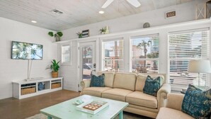 A living room with a beige sofa, a teal coffee table, and a TV on the wall.