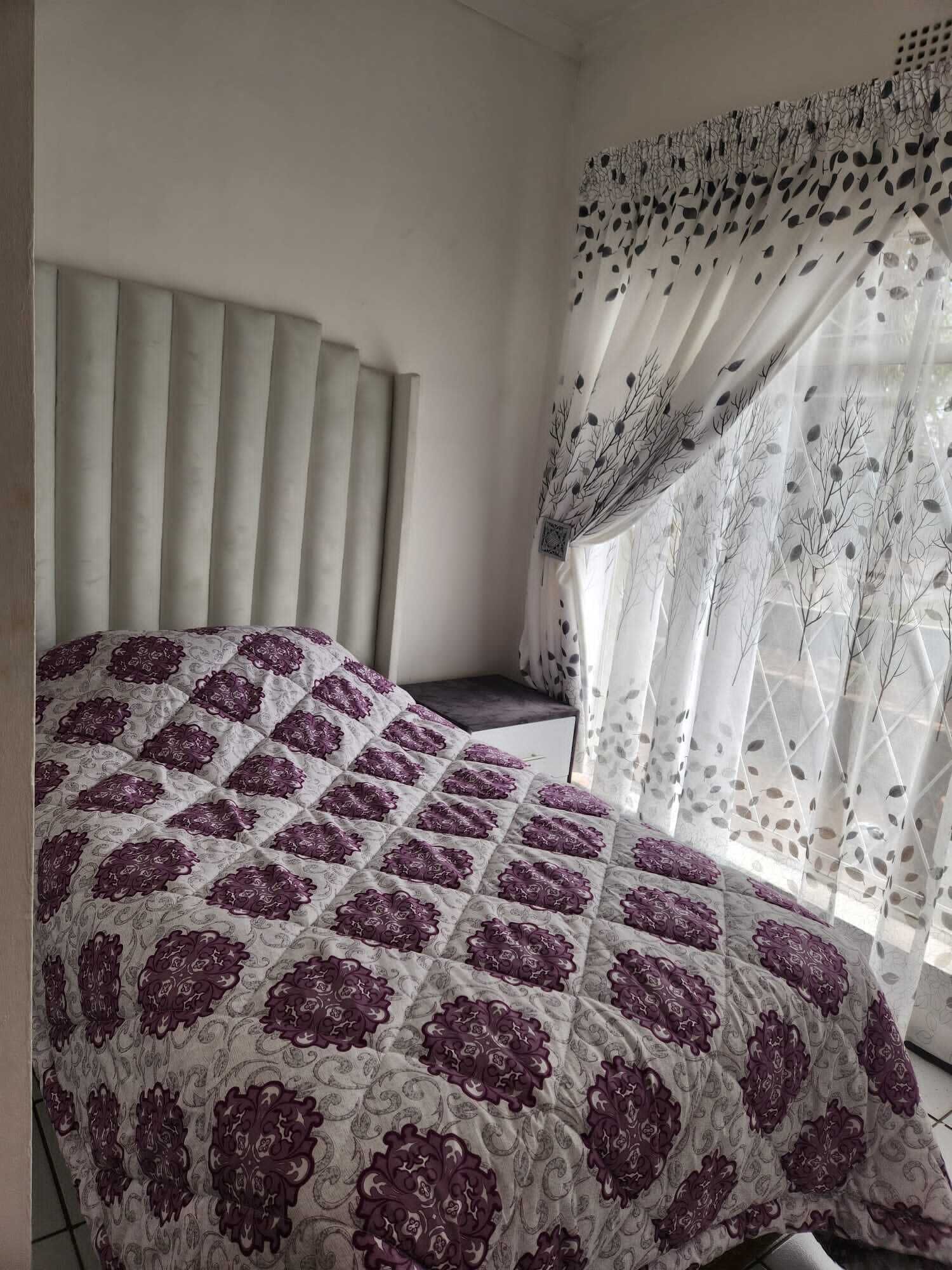 Un dormitorio con cama, cabecera y ventana con cortinas traslúcidas.